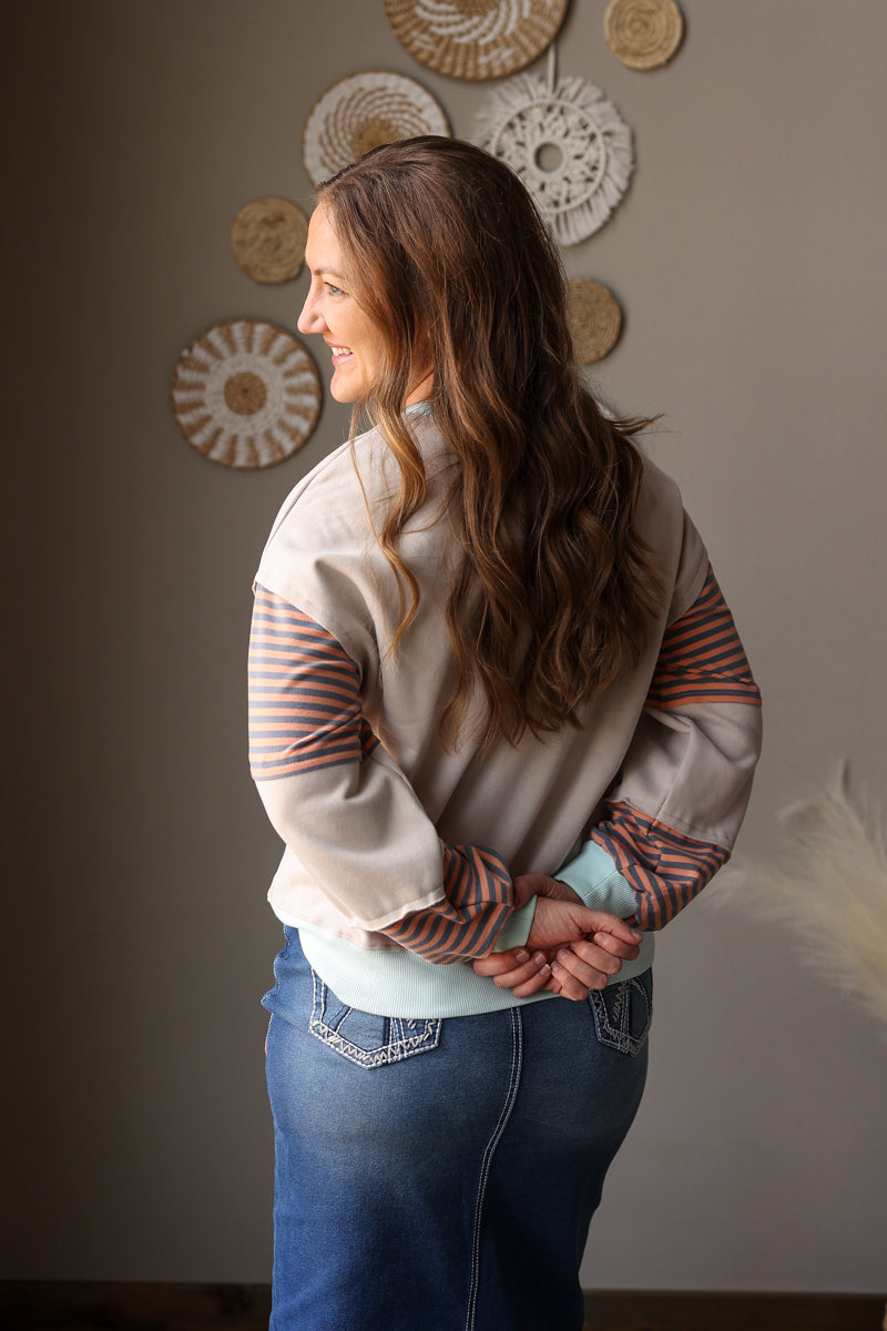 woman wearing a neutral tan sweatshirt with orange and mint colorblock detail with midi denim skirt for spring outfits and modest outfits