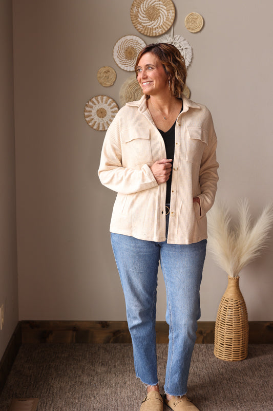 Woman wearing a beige shirt and blue jeans standing in a room with decorative wall art. Great shacket for easy cute and modest mom outfits at work or teachers. 