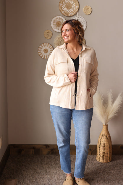Woman wearing a beige shirt and blue jeans standing in a room with decorative wall art. Great shacket for easy cute and modest mom outfits at work or teachers. 