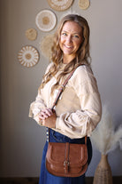 Angled close-up of a parchment sweatshirt with lace sleeve details and gathered cuffs, worn with a brown crossbody bag.