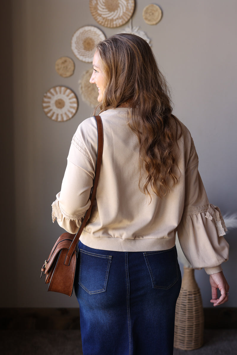 Back view of a parchment lace detail sweatshirt worn with a denim skirt and brown crossbody bag.