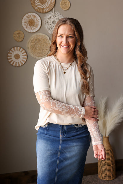 Woman wearing a white blouse with lace sleeves and blue jeans standing in a room with decorative wall art.