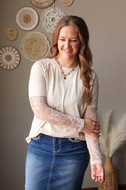 Woman wearing a white blouse with lace sleeves and blue jeans in a room with decorative wall art.