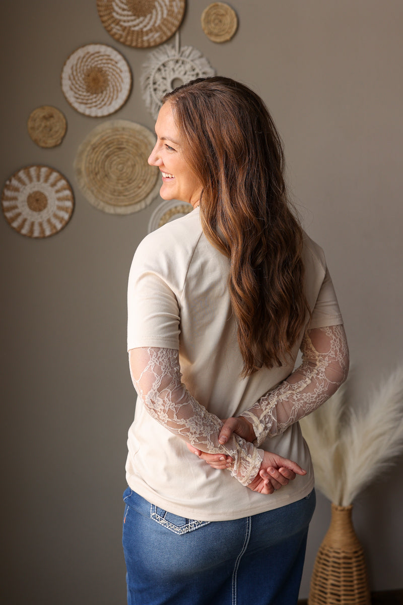 Woman wearing a beige lace top and blue jeans standing against a wall with decorative circular wall hangings.