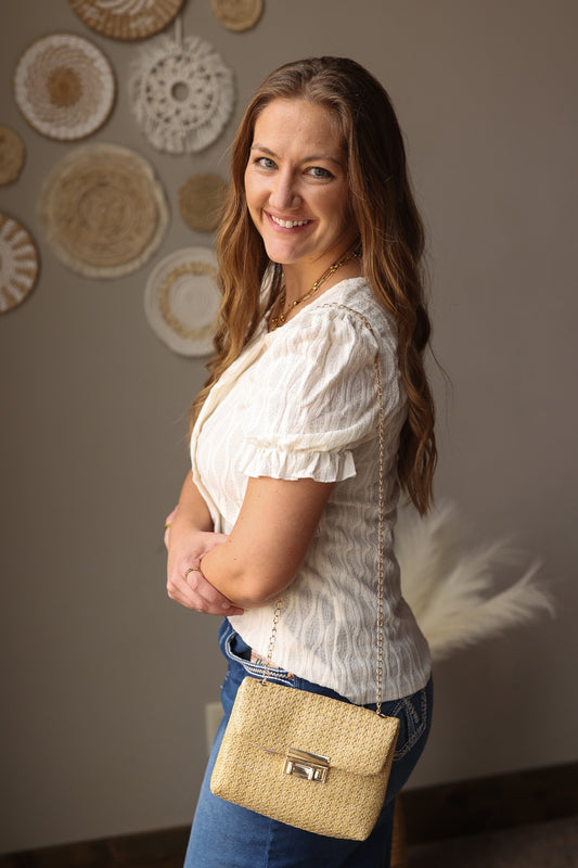 Woman holding a straw handbag in front of decorative wall plates, wearing a ivory blouse for Easter, spring, summer, church, office.