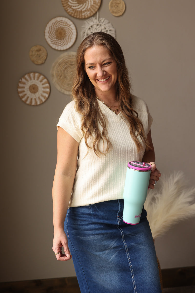 Woman holding a light blue tumbler with pink lid against a wall with decorative plates.