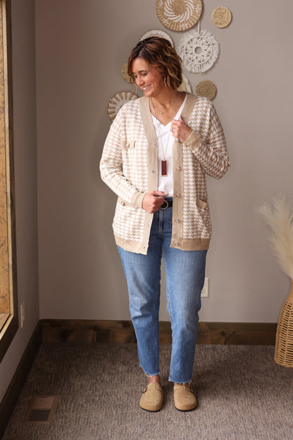 Woman wearing a beige cardigan, white shirt, blue jeans, and beige shoes in a room with decorative plates on the wall for fall winter 2025 fall winter outfits