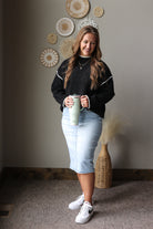 Full outfit view of a black stitch detail sweater with a light denim midi skirt and white sneakers.