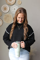 Close front view of a black mock neck sweater with light contrast shoulder stitching, worn with a light denim skirt.