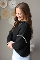 Side view of a black sweater highlighting the contrast stitching across the dropped shoulder and the ribbed sleeve cuff.