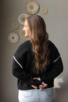 Back view of a black mock neck sweater showing the solid knit back and light stitch details at the shoulders.