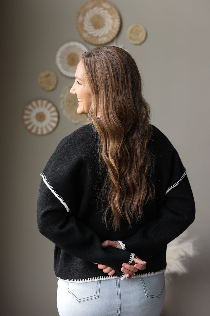 Back view of a black mock neck sweater showing the solid knit back and light stitch details at the shoulders.
