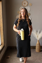 Woman in a black dress holding a yellow mug in a room with decorative wall art.