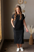 Woman wearing a black dress standing in a room with decorative wall art and a plant.