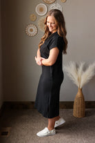 Woman in a black dress standing in a room with decorative wall art and a vase.