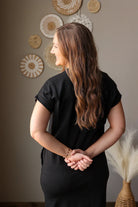 Woman in a black outfit standing in a room with decorative wall art.