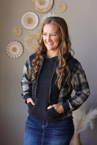 Front view of a black hoodie with grey plaid sleeves, drawstrings, and a front pouch pocket.