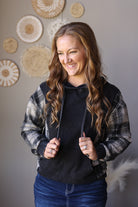 Black plaid sleeve hoodie shown with hands in the front pocket and a dark denim skirt.