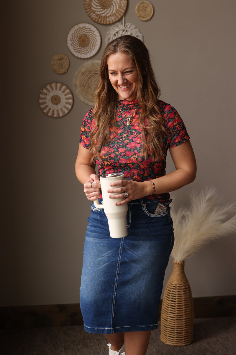 Woman holding a white tumbler with decorative wall and vase in the background