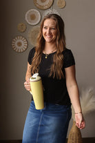 Woman holding a yellow tumbler with decorative wall art in the background