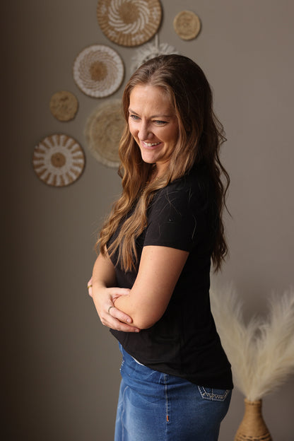 Woman in a black shirt and blue jean skirt standing against a wall with decorative plates.