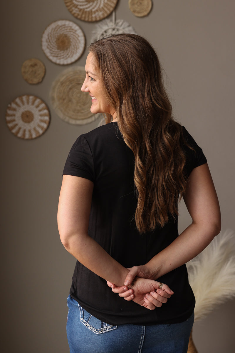 Woman wearing a black t-shirt and blue jean skirt standing against a wall with decorative circular objects.