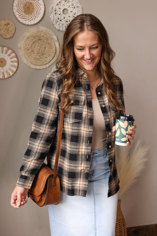 Black flannel button up top with a tan layer and light wash denim skirt on a women with a brown purse and latte coffee in hand. 