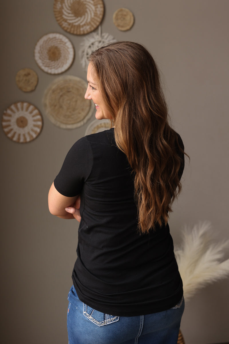 Woman wearing a black t-shirt and blue jeans standing in front of decorative wall art.