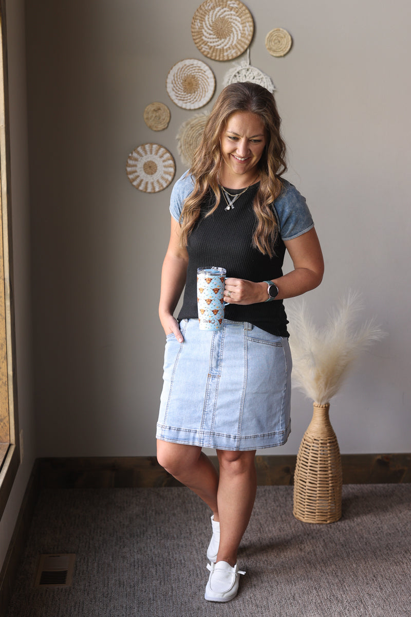 Woman standing in a room with decorative wall art, holding a cup.