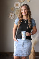 Woman holding a cup with a decorative sleeve in a room with wall art.