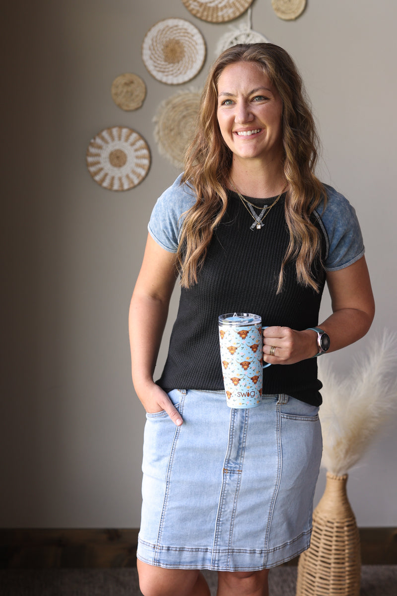 Woman holding a cup with a decorative sleeve in a room with wall art.