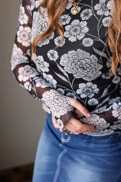 Person wearing a floral patterned top with lace details and blue jeans.
