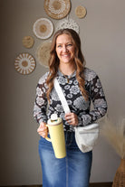 Woman holding a yellow water bottle with decorative plates on the wall behind her, wearing a black white floral mesh long sleeve top for spring. 