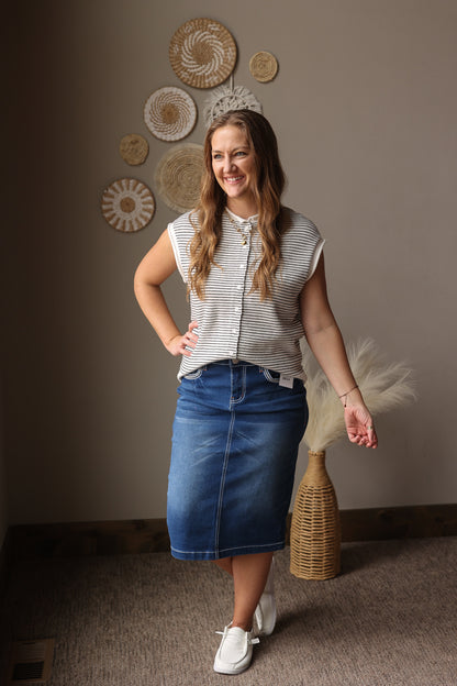 Woman in a striped shirt and denim skirt standing in a room with decorative wall art.