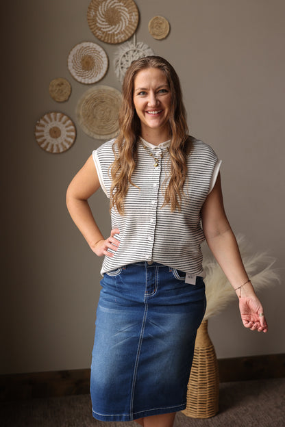 Woman wearing a striped shirt and denim skirt standing in front of decorative wall art.