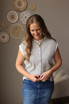 Woman wearing a striped shirt and blue jean skirt standing against a wall with decorative plates.