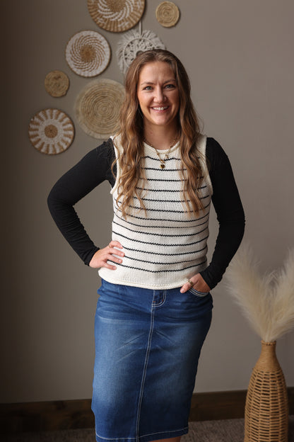 Woman wearing a striped sweater and denim skirt standing in a room with decorative wall art.