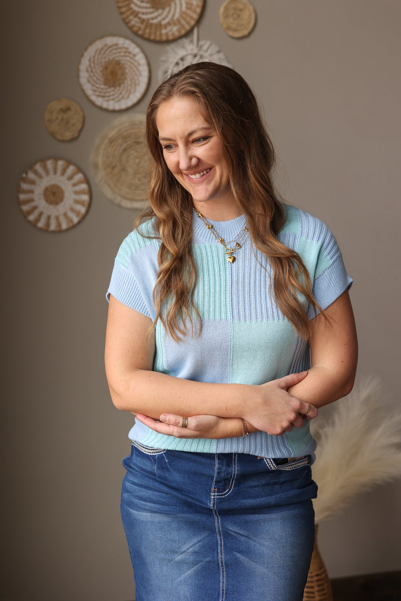 Woman wearing a light blue sweater and jeans standing in front of decorative wall art.