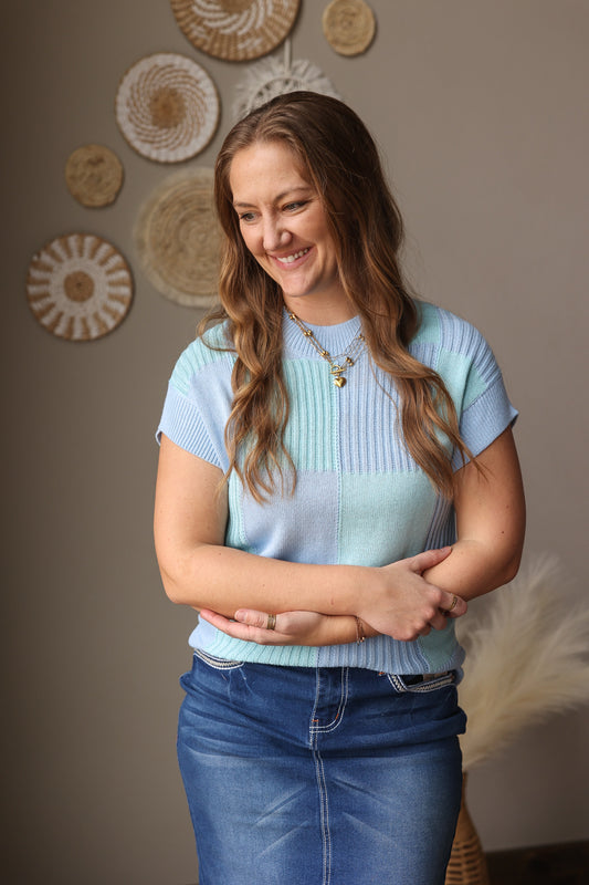 Woman wearing a light blue sweater and jeans standing in front of decorative wall art.