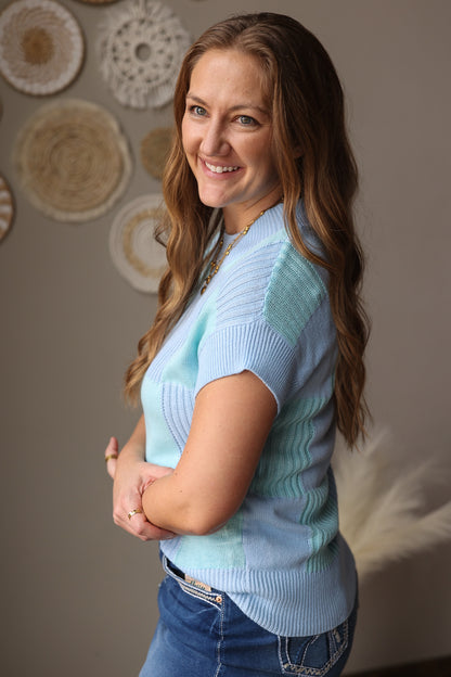 Woman wearing a light blue sweater vest with decorative wall plates in the background