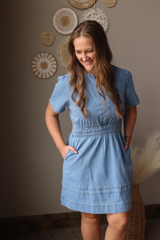 Woman wearing a blue dress standing against a wall with decorative plates.