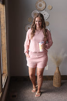 Woman in pink checkered pajama set holding a coffee cup in a room with decorative wall art.