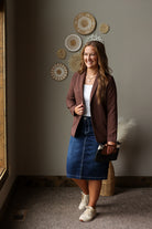 chocolate brown fully lined blazer with stretch styled with a dark wash denim skirt and sneakers, while she is holding a wristlet clutch purse