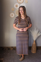 Woman wearing a striped dress standing in a room with decorative wall art and a vase.
