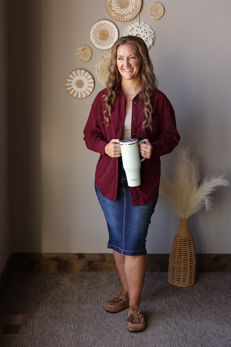 Full outfit view of a wine corduroy button shirt with a light top, denim midi skirt, and brown boots.