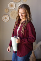 Angled front view of a wine corduroy pocket shirt layered over a light top while holding a pale tumbler.