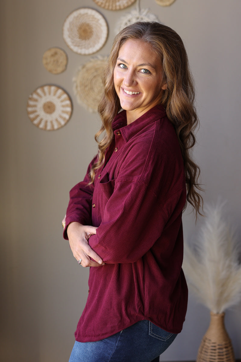 Side view of a wine corduroy shirt showing the sleeve and curved shirttail hem.