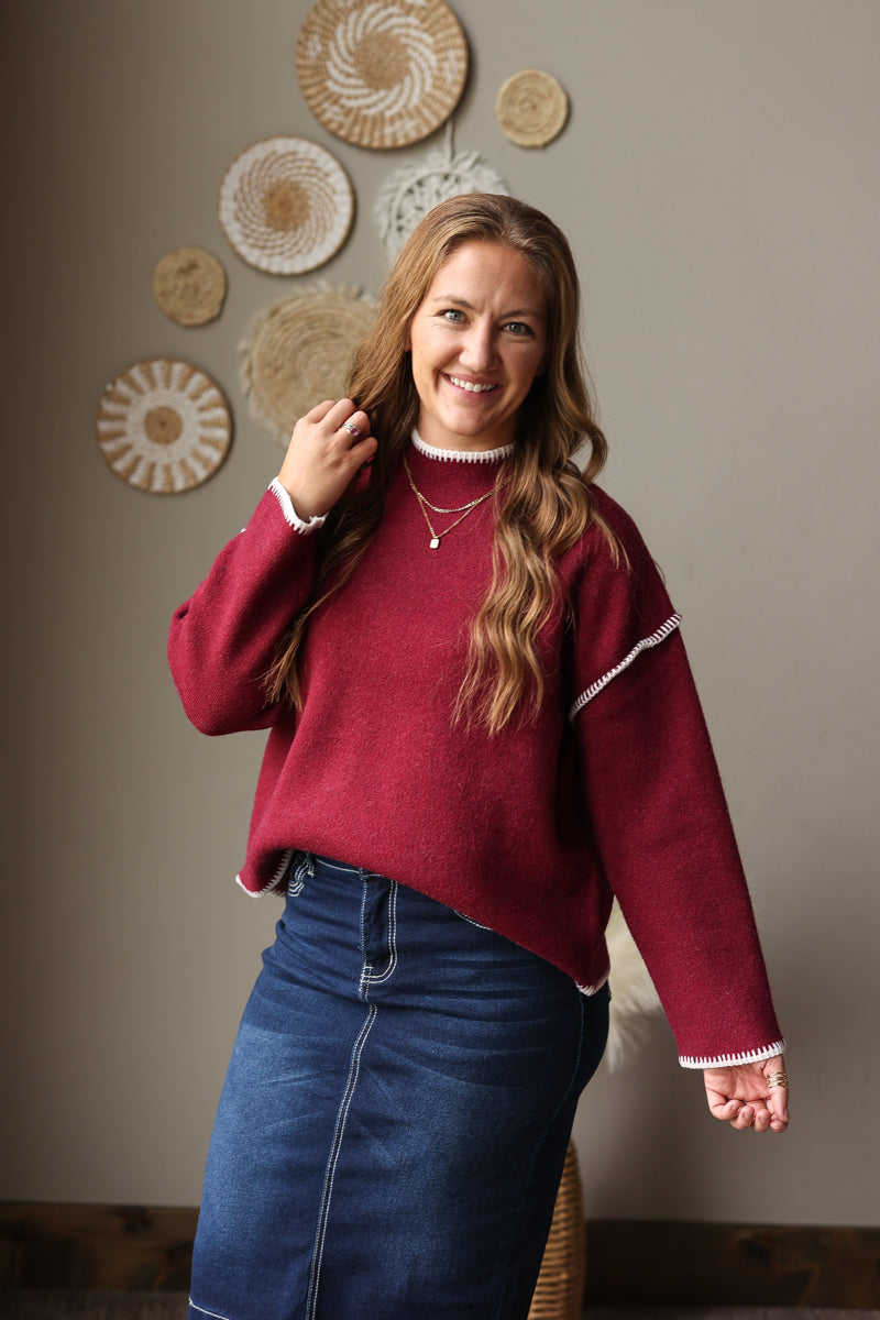 Cabernet long sleeve sweater worn with a dark denim skirt, showing light stitch trim and a ribbed hem.