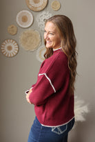 Side view of a cabernet mock neck sweater highlighting the light shoulder stitching and ribbed cuff.