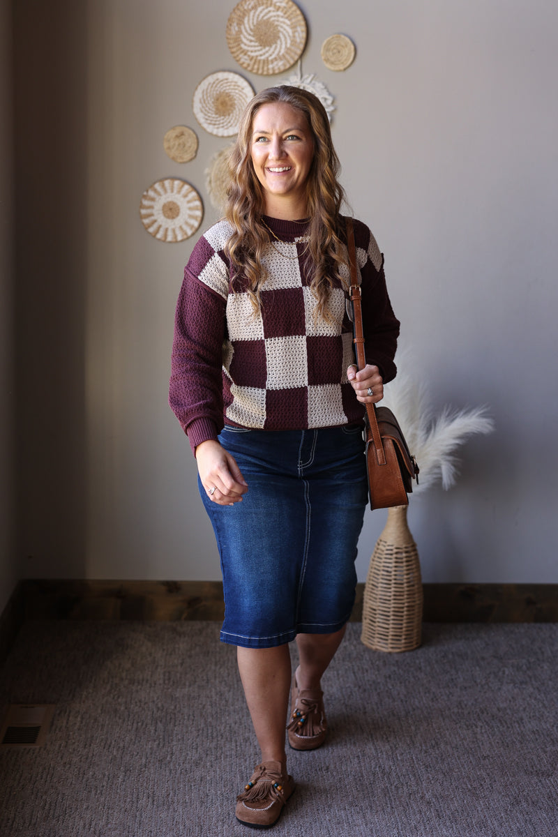 Brown and cream checkerboard sweater shown untucked over a denim midi skirt.